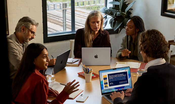 En gruppe med fem ansatte sitter rundt et møtebord og tre MacBook Pro brukes under møtet.