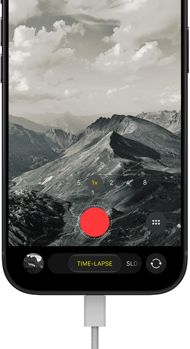 iPhone 18 Pro vises forfra. På skjermen er et fjellandskap, med kameramodus-overlay i tidsforløp-modus, med strømkabel festet til ladeporten