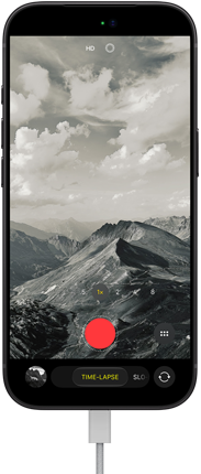 iPhone 18 Pro vises forfra. På skjermen er et fjellandskap, med kameramodus-overlay i tidsforløp-modus, med strømkabel festet til ladeporten